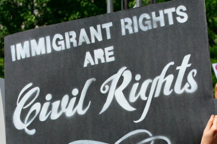 a hand holds a black sign with white chalk text: "immigrant rights are civil rights"