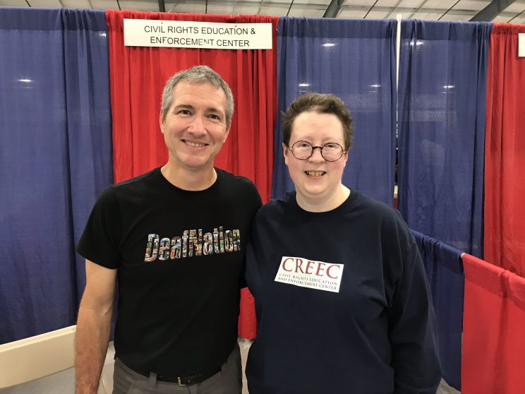 Joel Barish CEO of DeafNation with Martie. Joel is a white man in a black t-shirt with the DeafNation logo on it. Martie is a white woman wearing a blue Disability Law United shirt. 