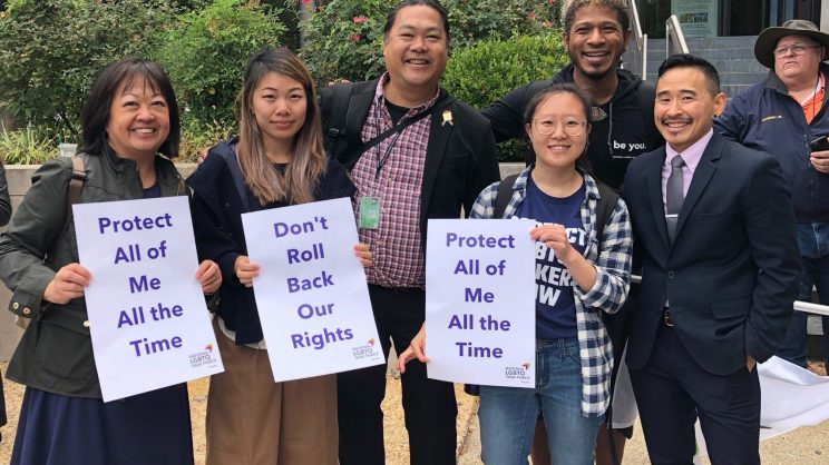 Group of protesters at a rally holding signs that read "Protect All of Me All the Time" and, "Don't Roll Back Our Rights"
