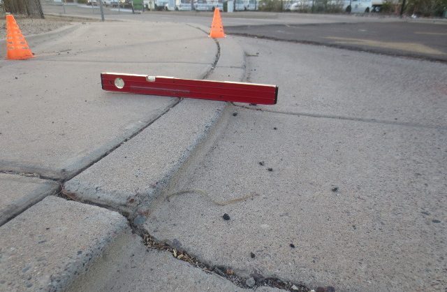 close up of a builder's level showing an unsafe curb ramp access point and a large crack