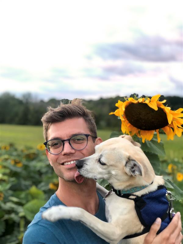 Man holding dog in front of sunflower