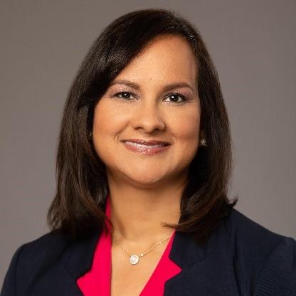 A headshot of Martha Bahamón, a woman with shoulder-length brown hair who is smiling against a gray background.